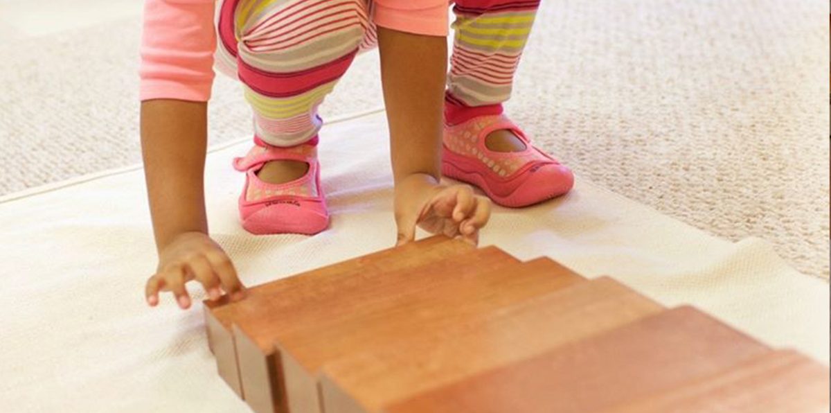 Bambino che manipola con cura i prismi in legno massello della scala marrone